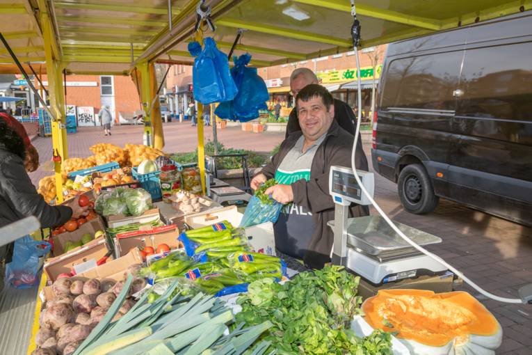 Kundschaft und Verkäufer an einem Marktwagen mit Gemüse.